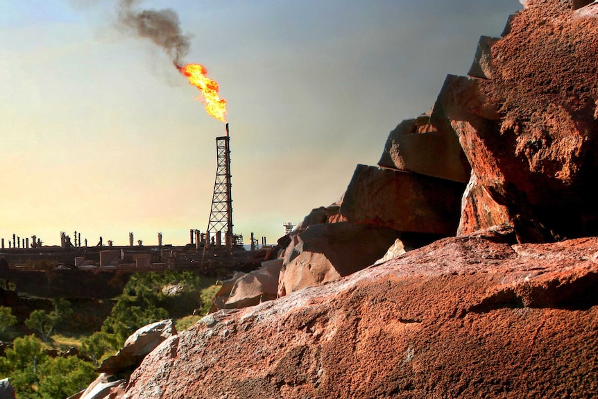 A gas derrick burns in the background, with rocks and rock art visible in the foreground