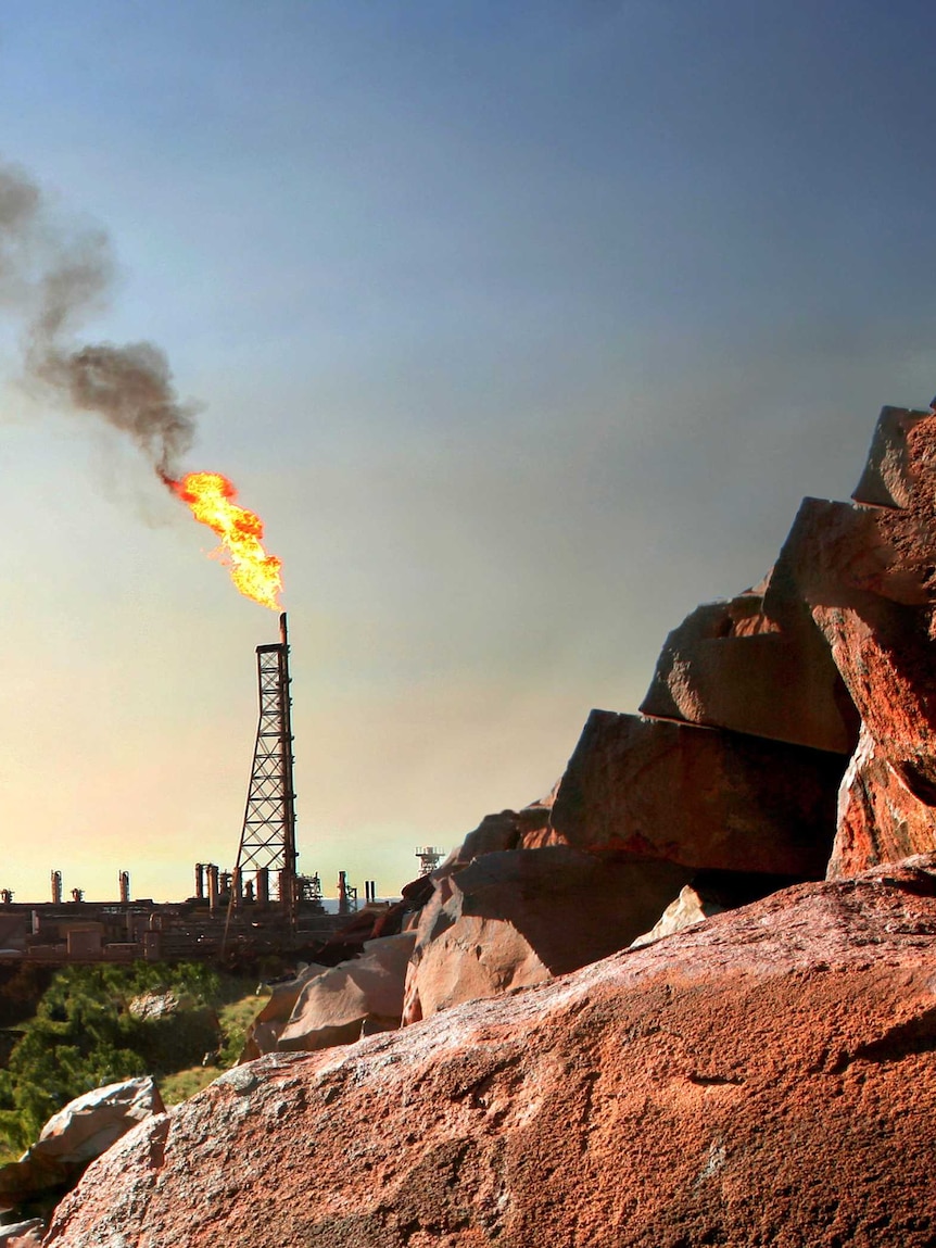 Red rocks with engravings at Burrup Peninsula, with a gas derrick burning in the background