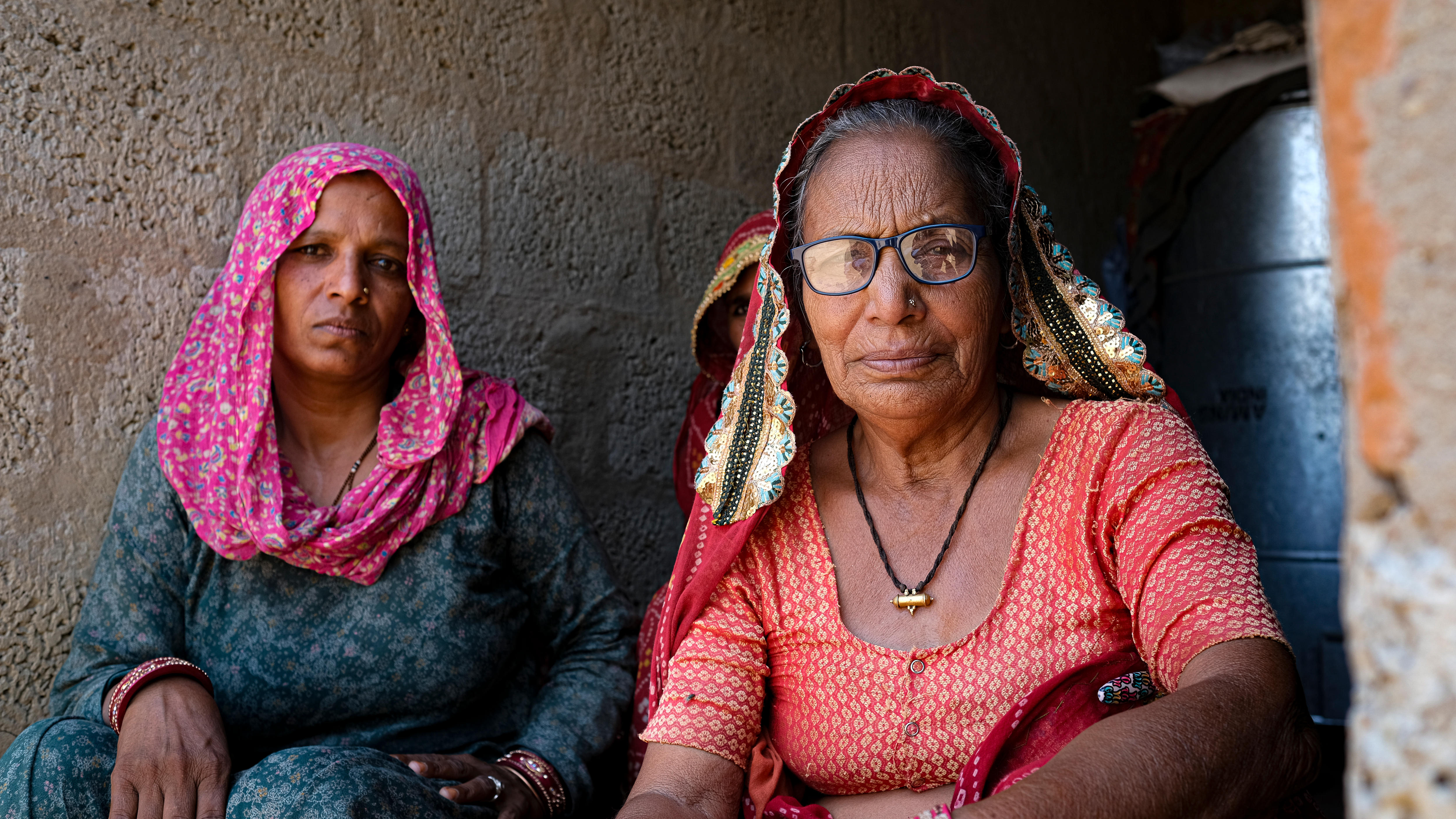 Two women sit side by side look into the camera with solemn expressions.