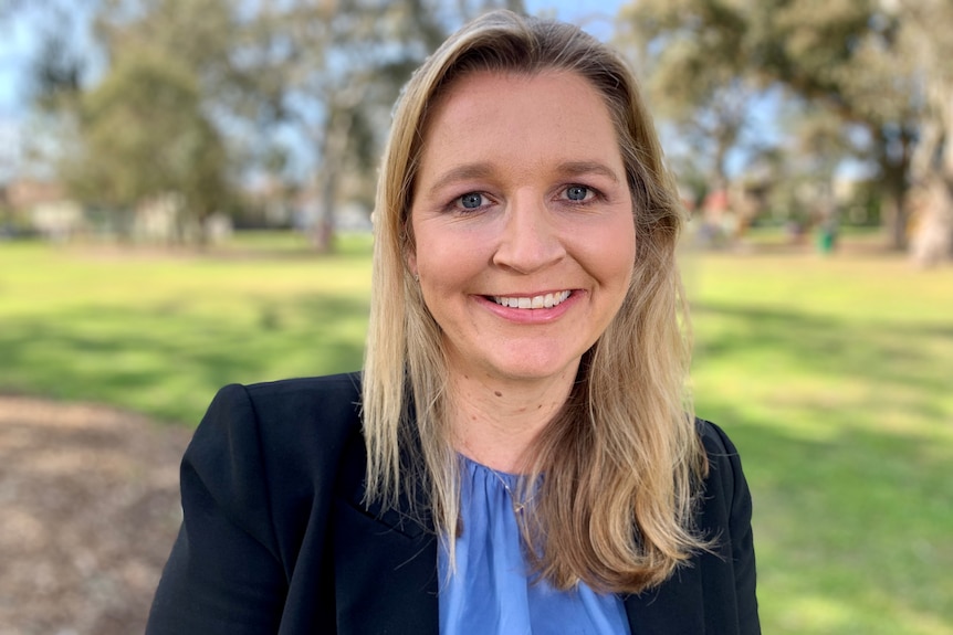 A woman in a black jacket smiling at a park.