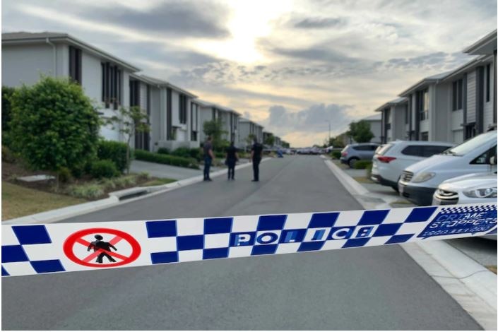 Police tape in the foreground with three police standing together on the street beyond