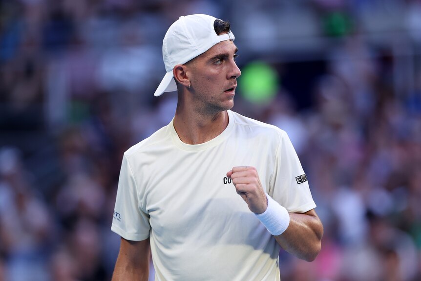 A male tennis player, in a light shirt, holds a clinched fist in celebration, looking at a crowd