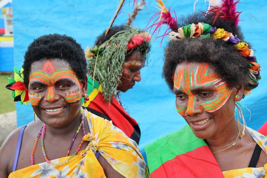 Two Ni-Vanuatu women in traditional head-dress and colourful traditional markings on their faces.