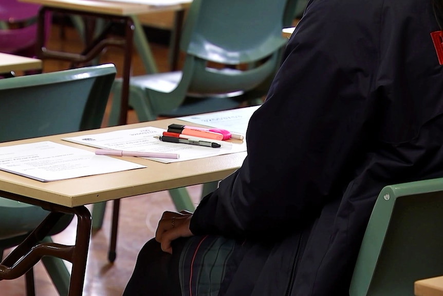 a student sitting at a desk with paper and pens on the table