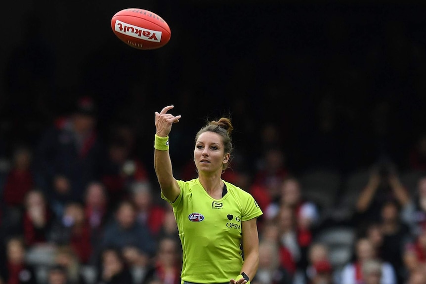 A female umpire tosses the ball in an AFL match.