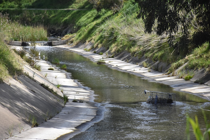 A stream lined with concrete with a shopping cart half immersed in
