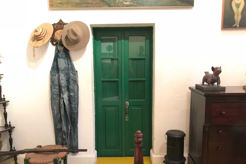 A view inside Diego Rivera's bedroom. A green bathroom door is in the centre of the room. Beside it hang overalls and hats.