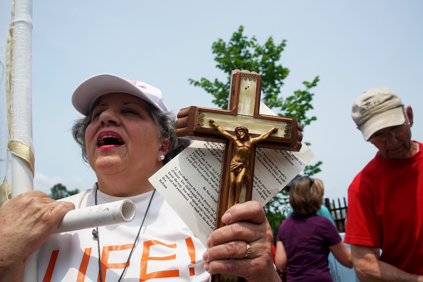 A woman holds a crucifix.