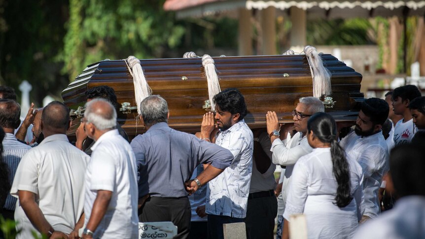 Men dressed in white shirts carry a wooden coffin.