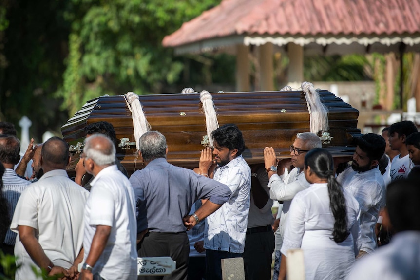 Men dressed in white shirts carry a wooden coffin.