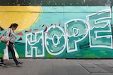 A woman wearing a mask carrying shopping walks past HOPE graffiti painted on a wall in a street in Sydney 