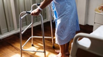 A person wearing a blue hospital gown with a walking frame.