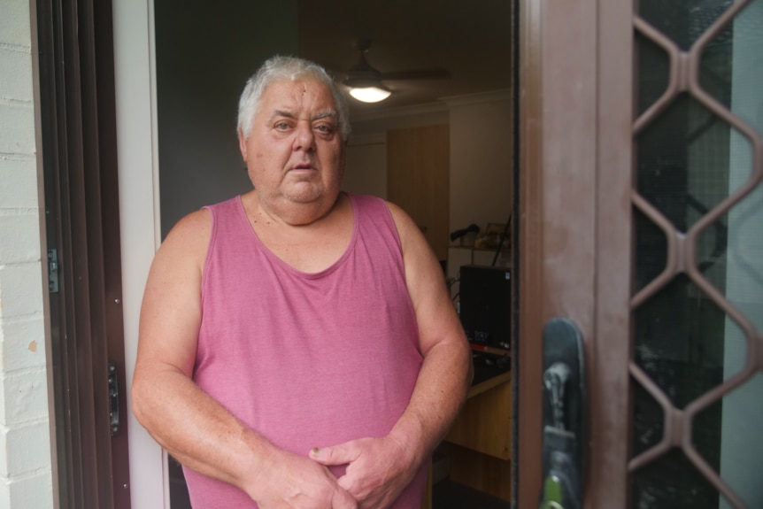 A man in a singlet stands in his doorway.