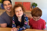 Marc Fennell and two young kids sit at a dining room table with plates of cupcakes, smiling.