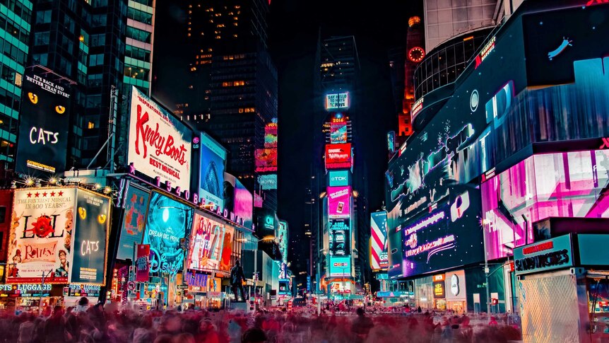 Crowds rush through neon lights and bright signs in Times Square in New York at night.