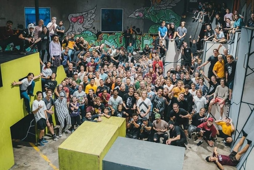 A large community of parkour athletes pose in front of the indoor course.