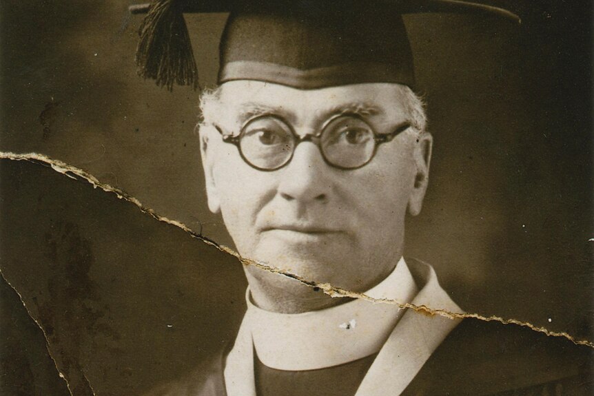 A black and white photo of a man wearing glasses, a mortar board and gown