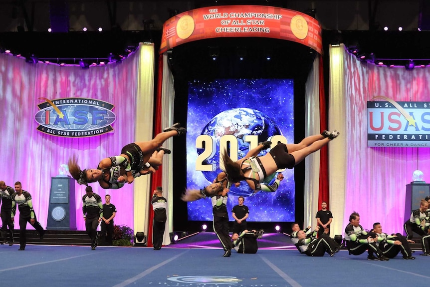 Three cheerleaders in mid air in front of their team during a competition.