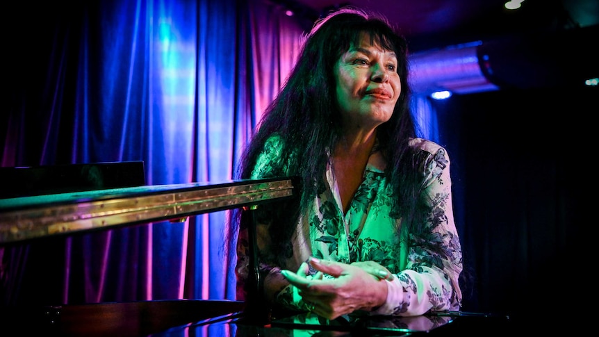 Wilma Reading leaning on a piano in a dark room at a Sydney jazz club.