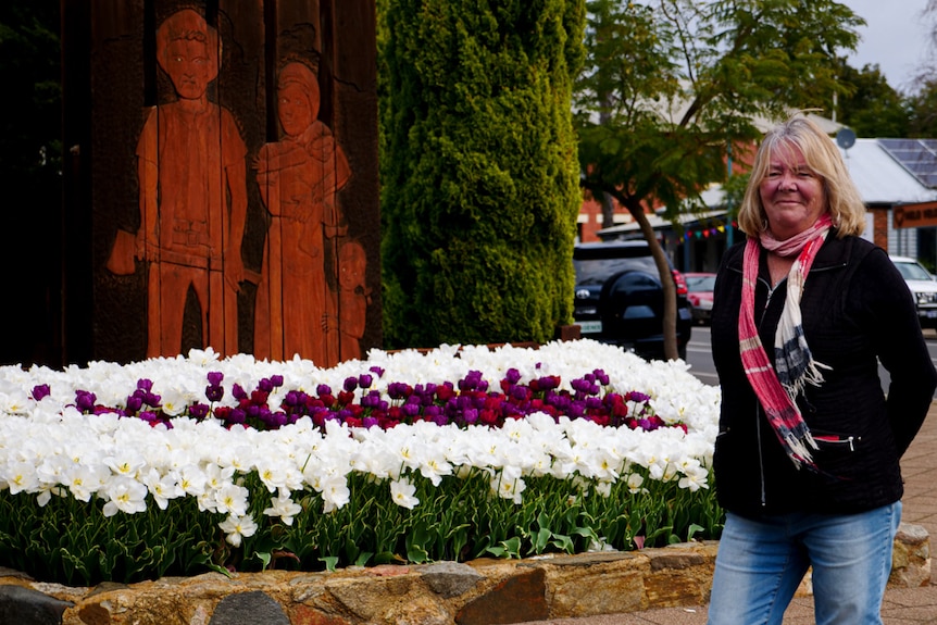 A woman smiling standing near a garden bed of flowers