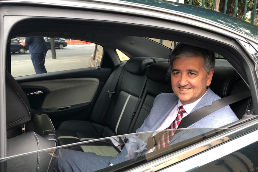 Rob Lucas smiles from the back seat of a car.