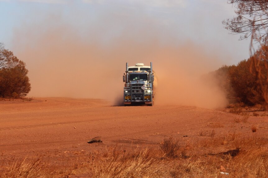 A road train travels the Outback Way, throwing up dust
