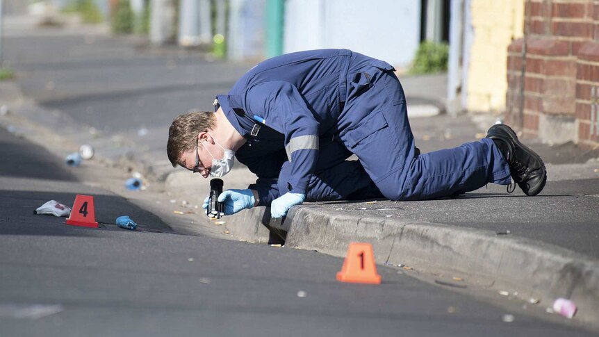 A forensic police officer shines a torch into a drain at the crime scene.