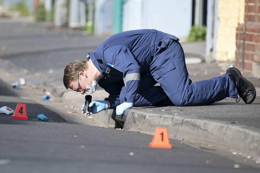 A forensic police officer shines a torch into a drain at the crime scene.