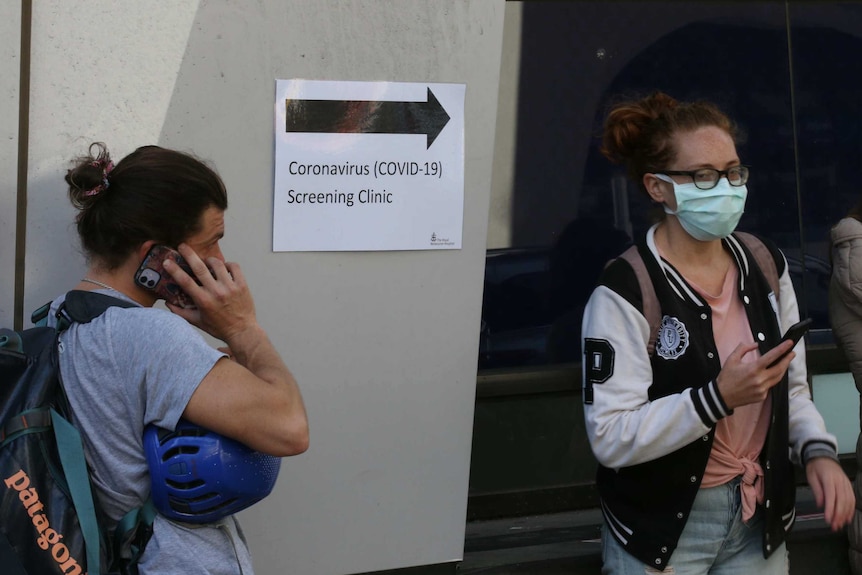 Two people stand outside a sign pointing to a coronavirus screening clinic