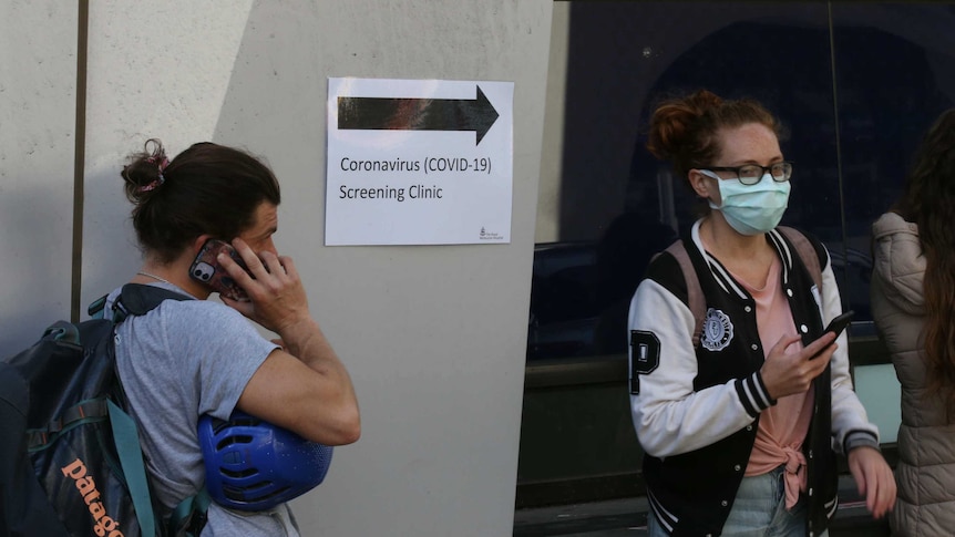 Two people stand outside a sign pointing to a coronavirus screening clinic