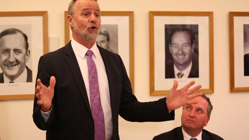Nigel Scullion speaks while Barnaby Joyce, who is seated nearby, looks up at him.