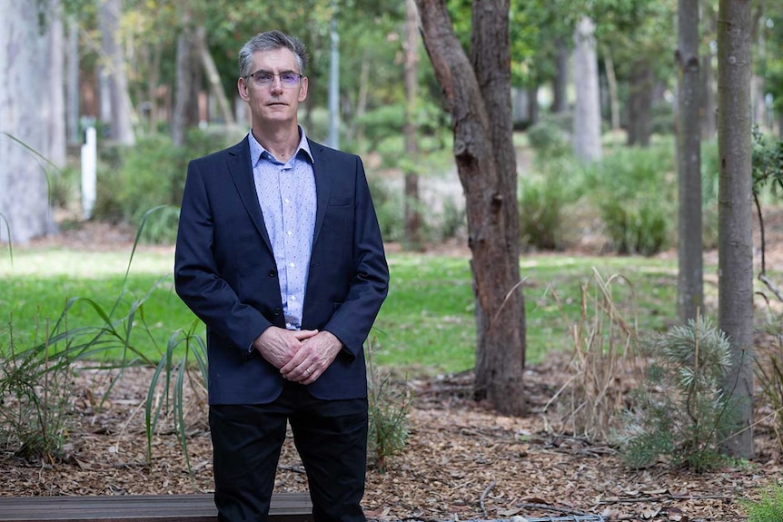 Craig Dalton stands in a garden, looking straight toward the camera.