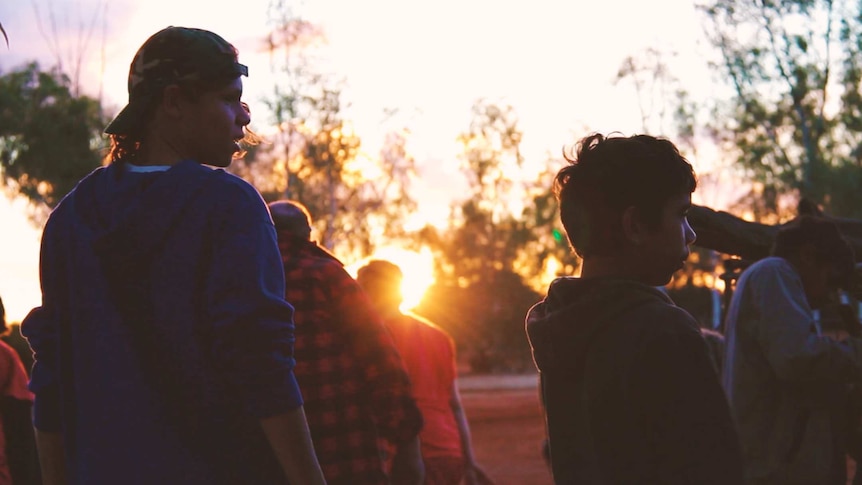 Aboriginal boys look over a paddock as the sun sets