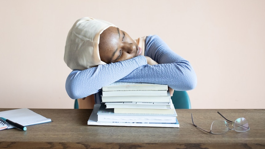 A woman asleep with her head on a pile of books for a story on sleep centres. 