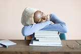 A woman asleep with her head on a pile of books for a story on sleep centres. 