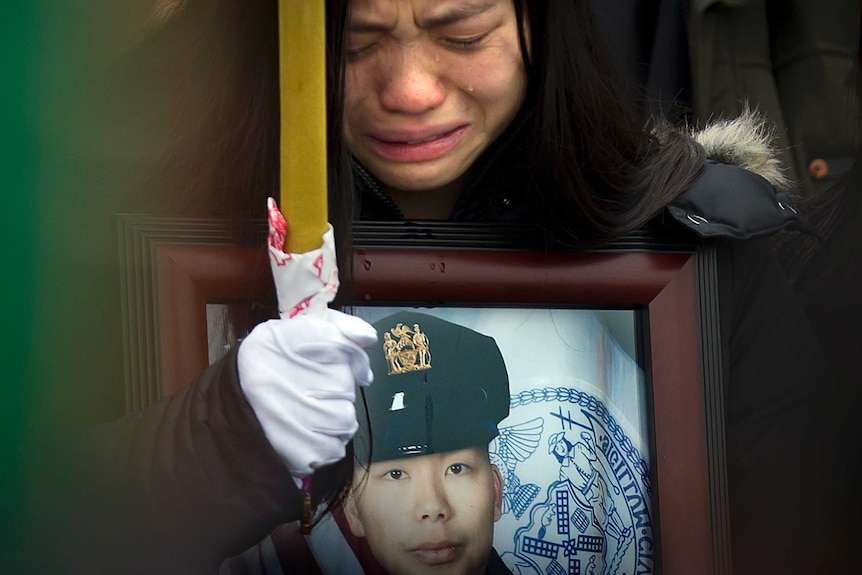 A close shot of widow, Pei Xia Chen, crying as she holds a portrait of her slain husband, Wenjian Liu.