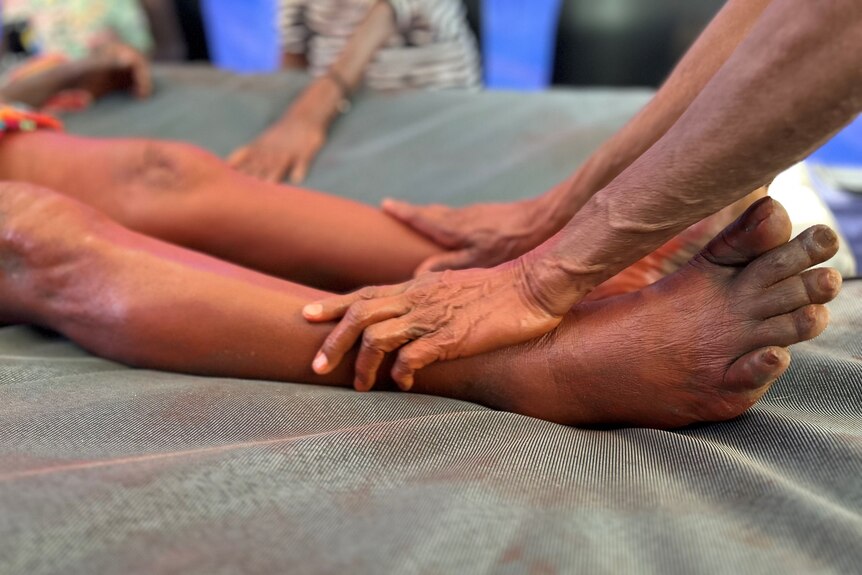 A woman's hands massaging red ochre paint into another woman's legs