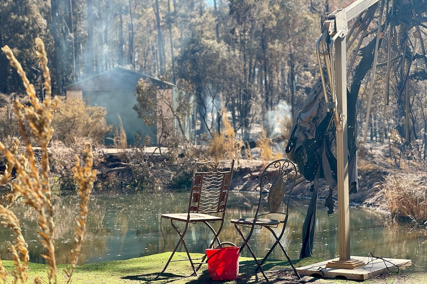 Two burnt metal chairs next to a burnt umbrella looking out at the look with smoke in the background.