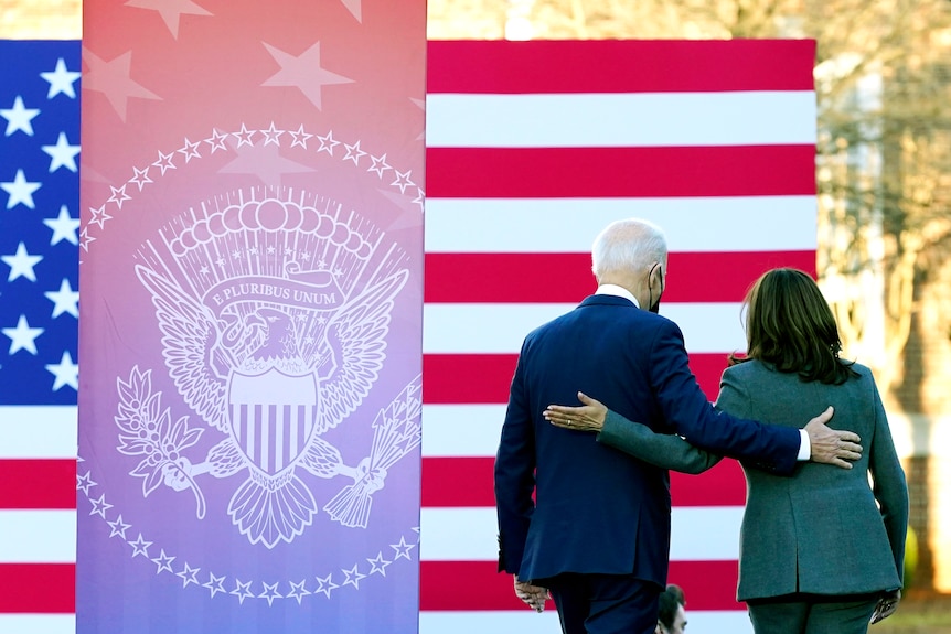 Joe Biden and Kamala Harris walk away from the camera with their arms around each other