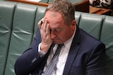 Barnaby Joyce clasps his right hand — which is already clutching a pen — to his face. He looks exhausted.