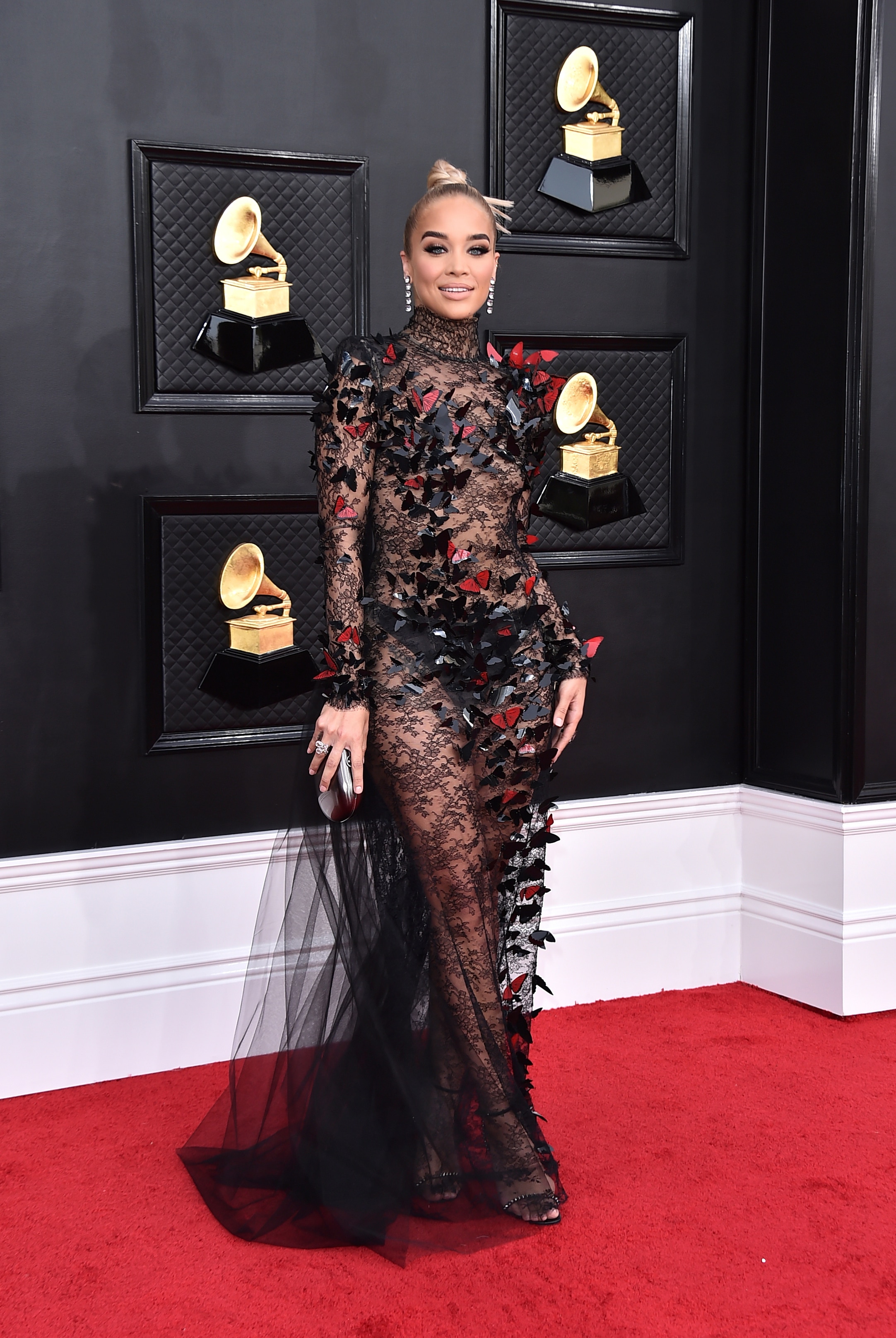jasmine sanders poses on the grammys red carpet wearing a sheer black lace dress with black and red butterfly accents