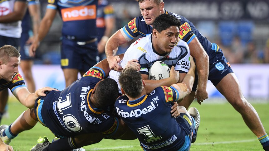 Jason Taumalolo carries the ball under his arm with three Titans players in blue shirts around him