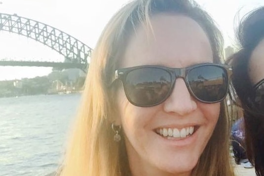 A selfie of a woman in sunglasses smiling in front of the Harbour Bridge. 