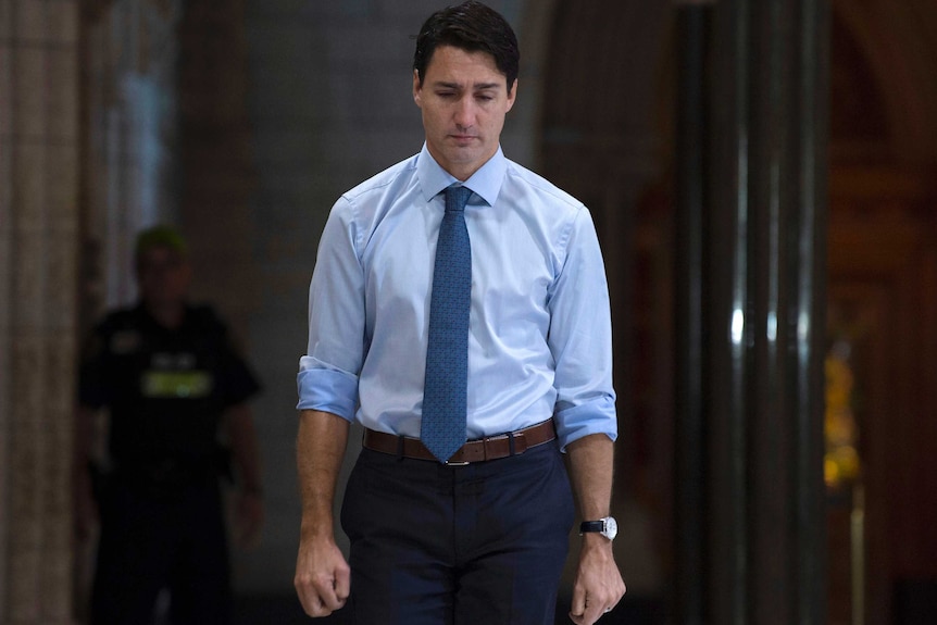 A sad-looking Justin Trudeau walks down a hall.