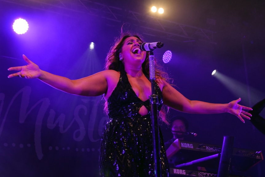 A woman holds her hands out to the side as she sings into a microphone.