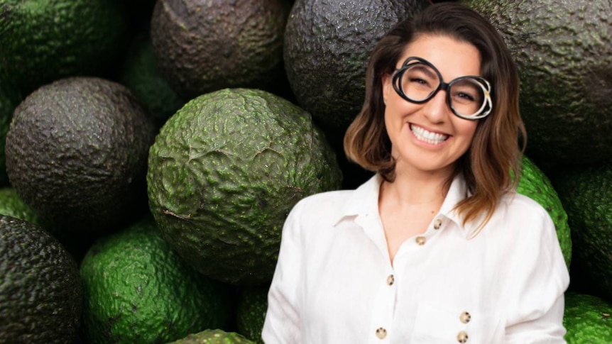Composite picture of a woman smiling in front of whole lot of avocados. 