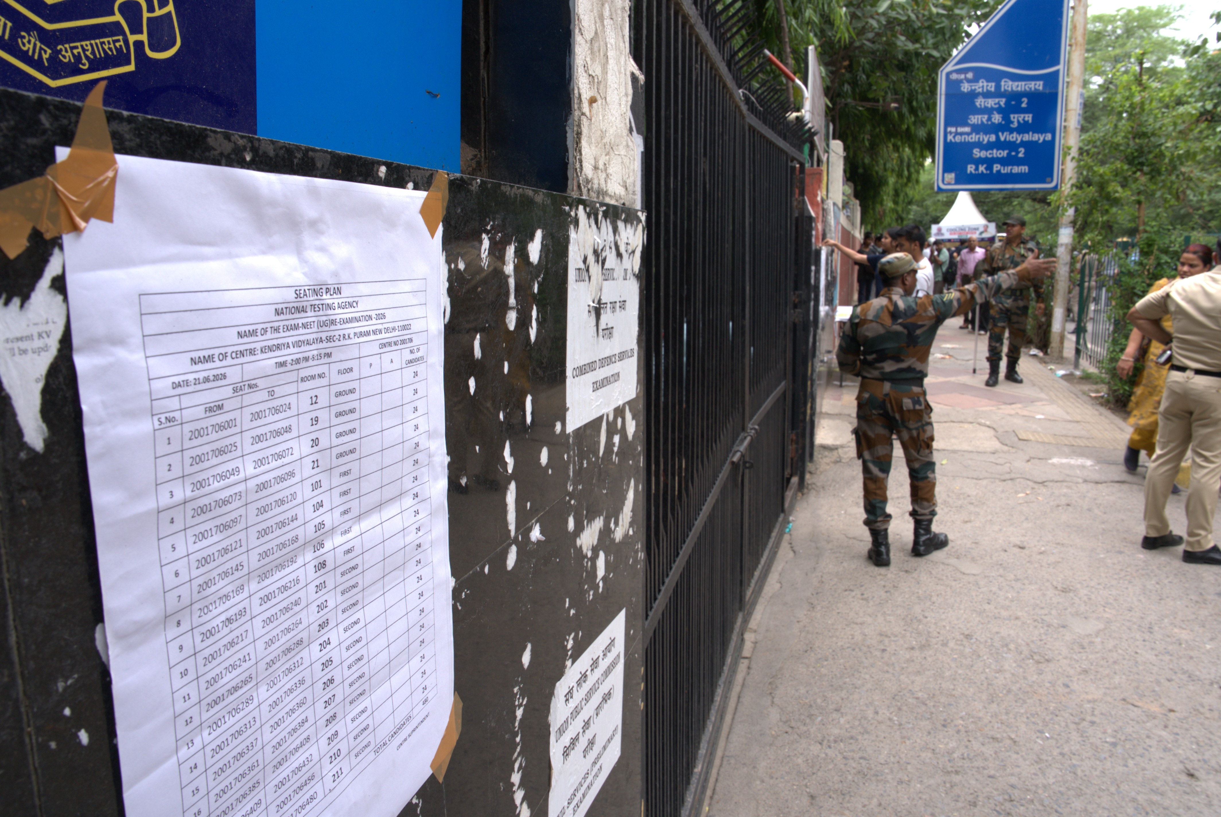 A list of exam rooms on a wall outdoors, with a soldier waving his arm.