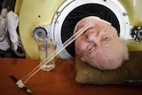 Polio survivor Paul lying down in an iron lung with a glass of water next to his head
