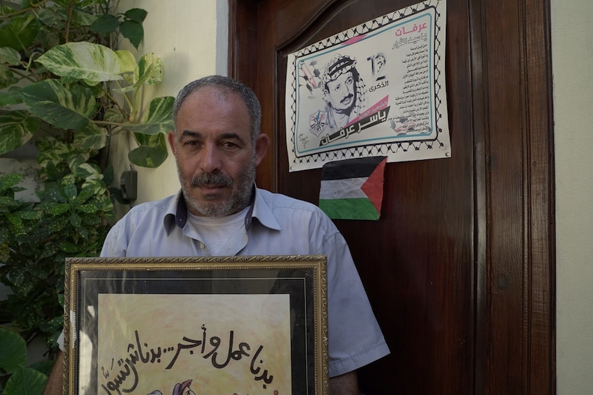 Salah Abed, a Palestinian refugee holds a sign with Arabic writing and a drawing.