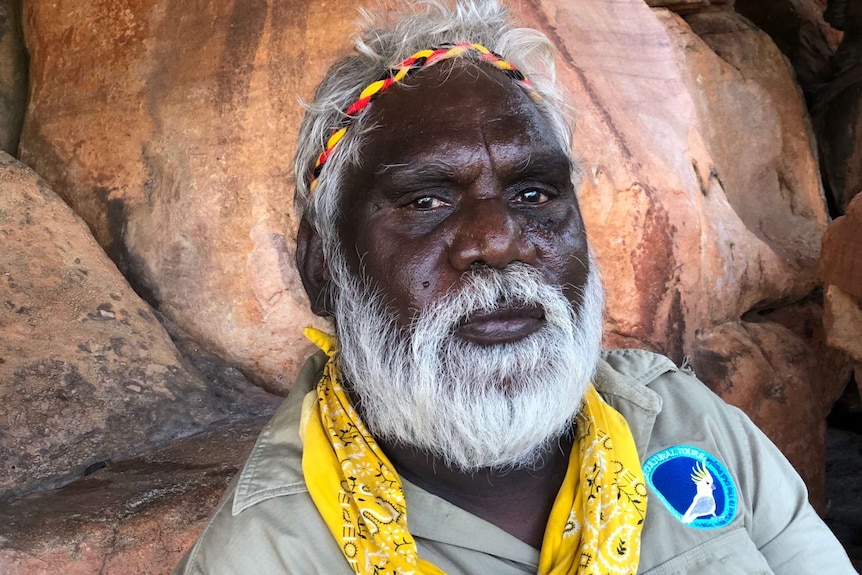 Clarrie Djanghara sitting in front of a rock wall.